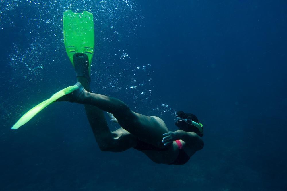 Snorkeler diving deep with green fins in blue ocean.