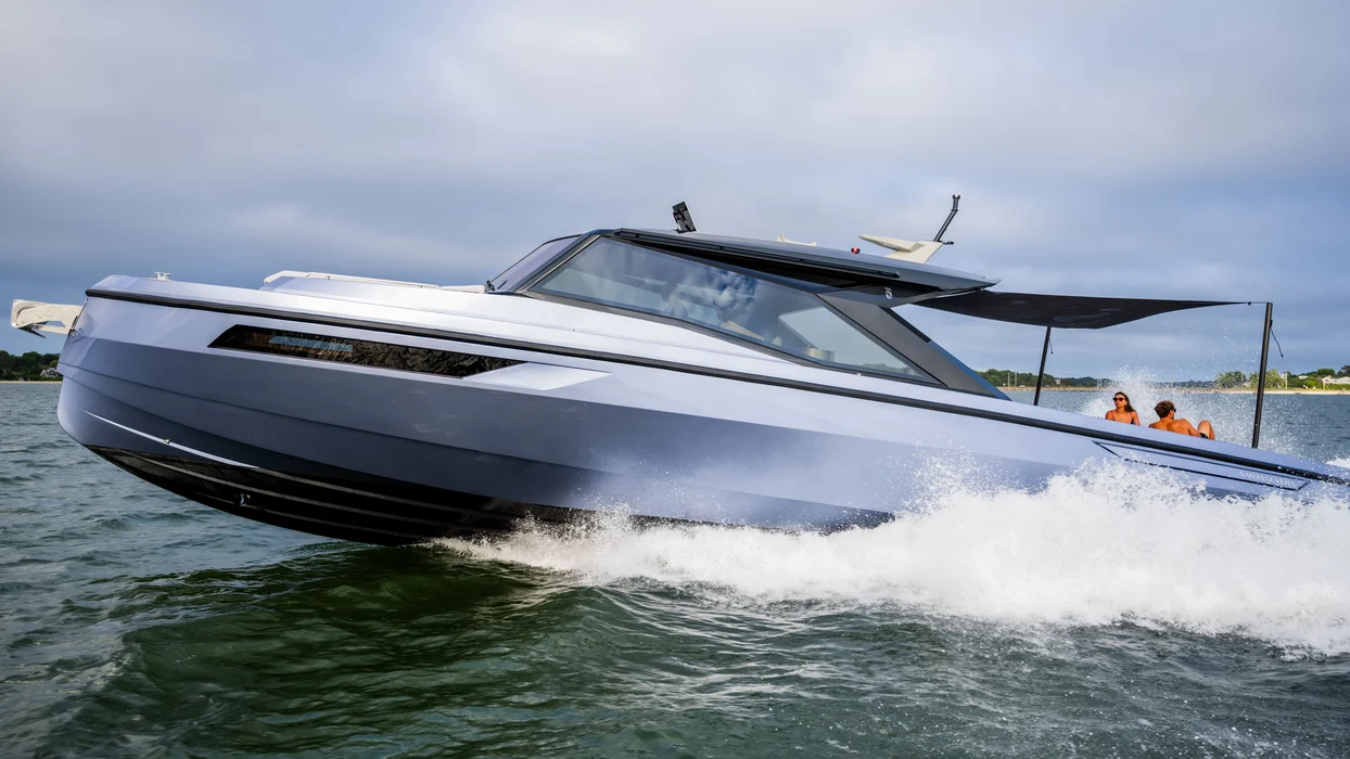 Luxury yacht speeding past shoreline under cloudy coastal sky.