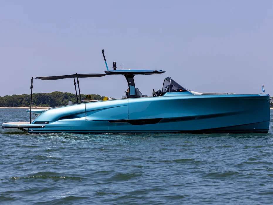 Turquoise-hulled yacht anchored near forested shoreline on sunny day.