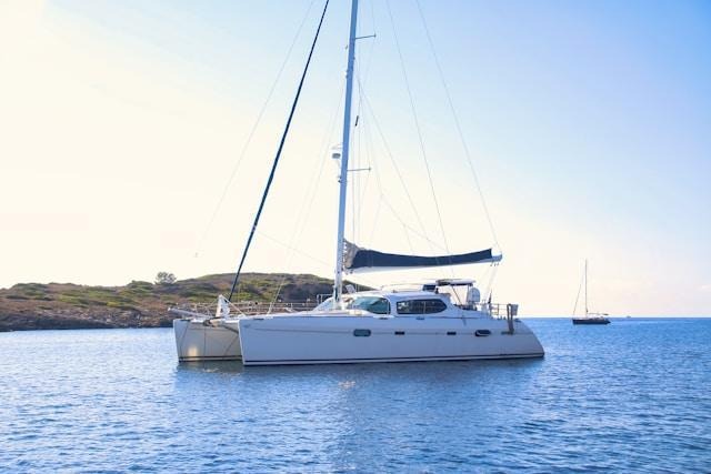 White catamaran anchored near rocky shoreline under clear sky.