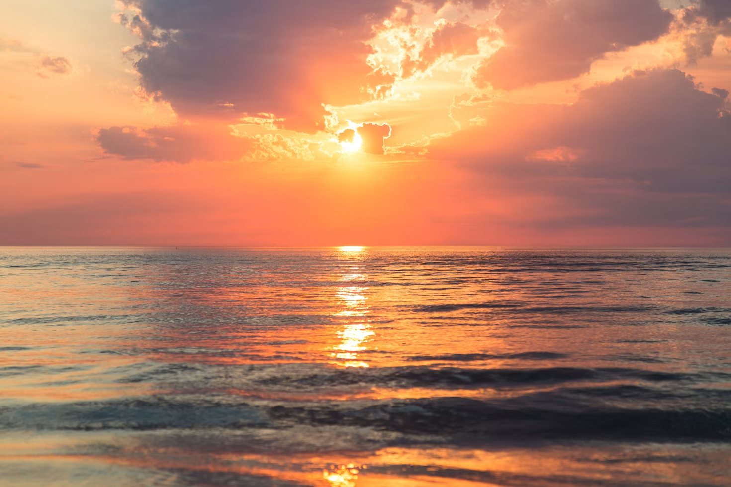 Golden sunset reflecting on calm ocean with scattered clouds.