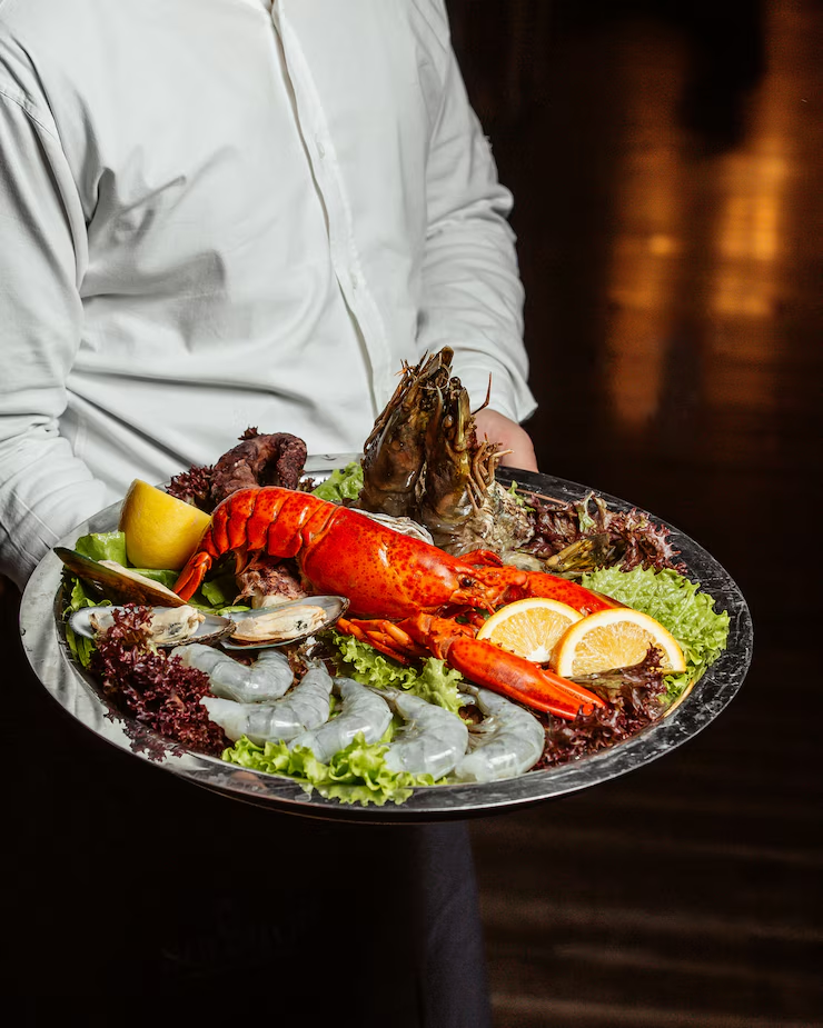Waiter holding seafood platter with lobster, king prawns, and mussels