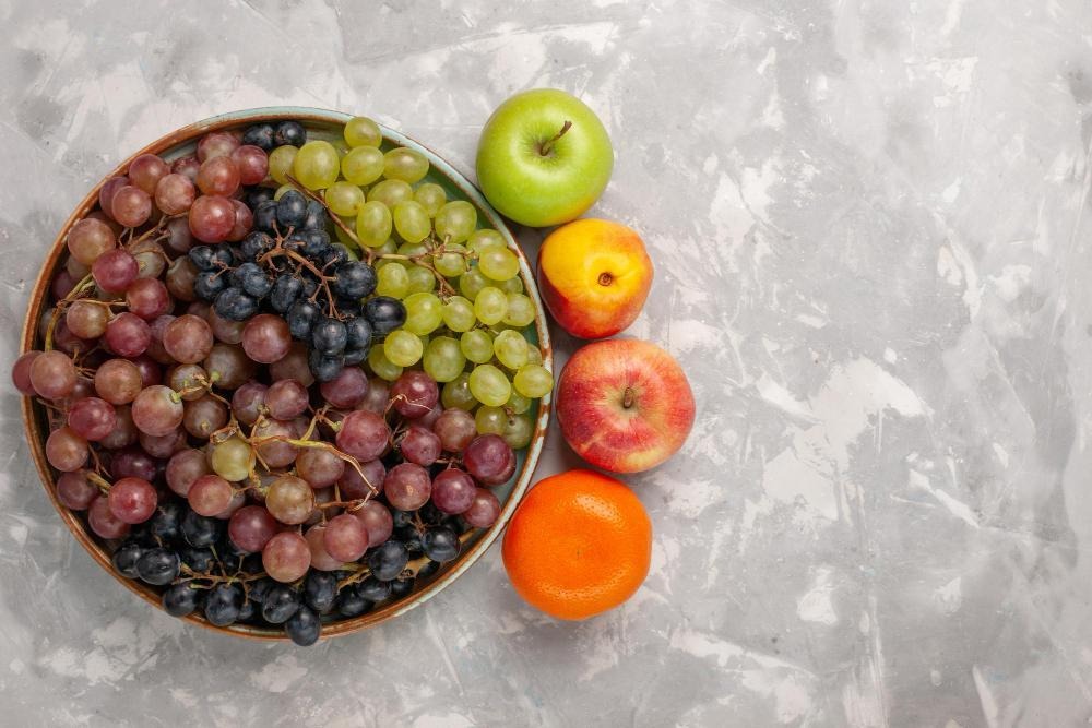 Plate of grapes beside assorted whole fruits on the surface.