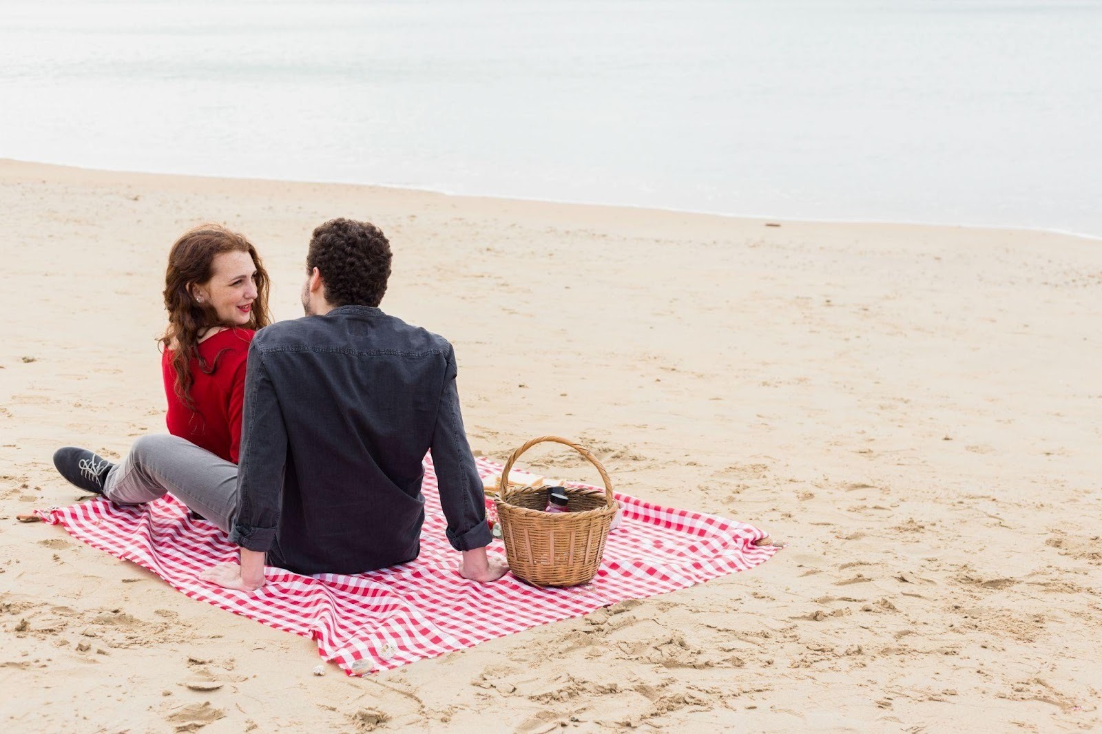 Couple enjoying romantic beach picnic on checkered blanket.