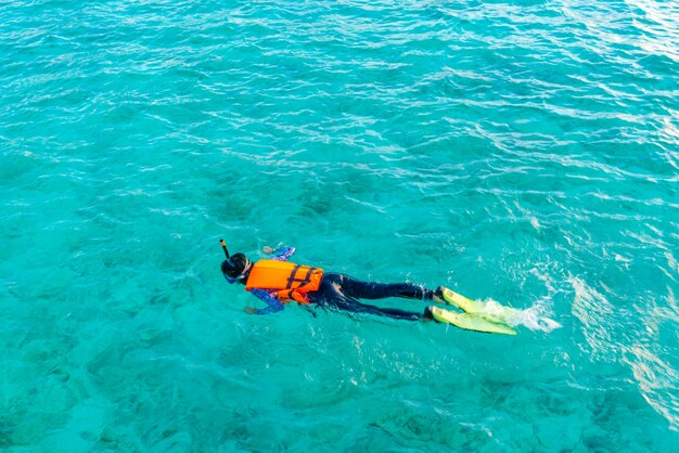 Person snorkeling in clear turquoise water with mask, fins, and life vest.