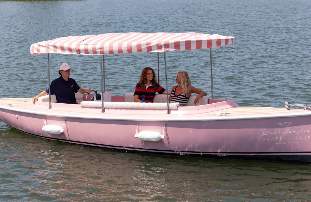 Three people cruising a pink leisure boat under a striped canopy.