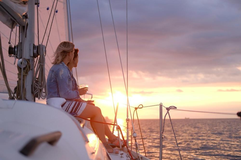 Two people enjoying drinks on a sailboat at sunset.