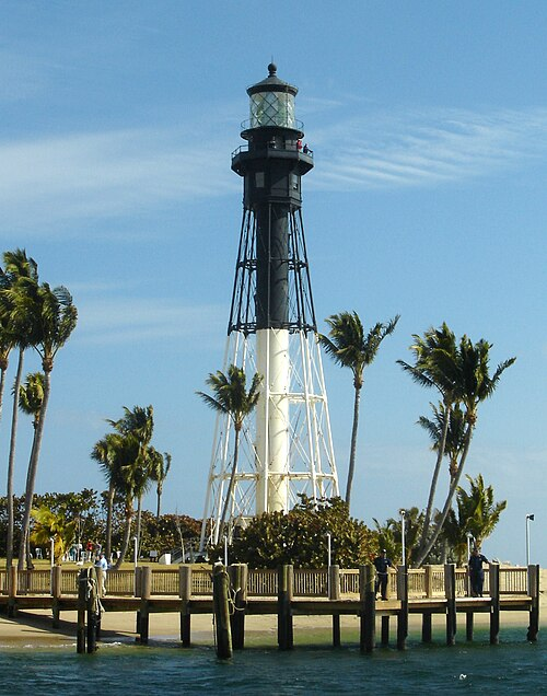 Historic Hillsboro Inlet Lighthouse surrounded by palm trees and pier.