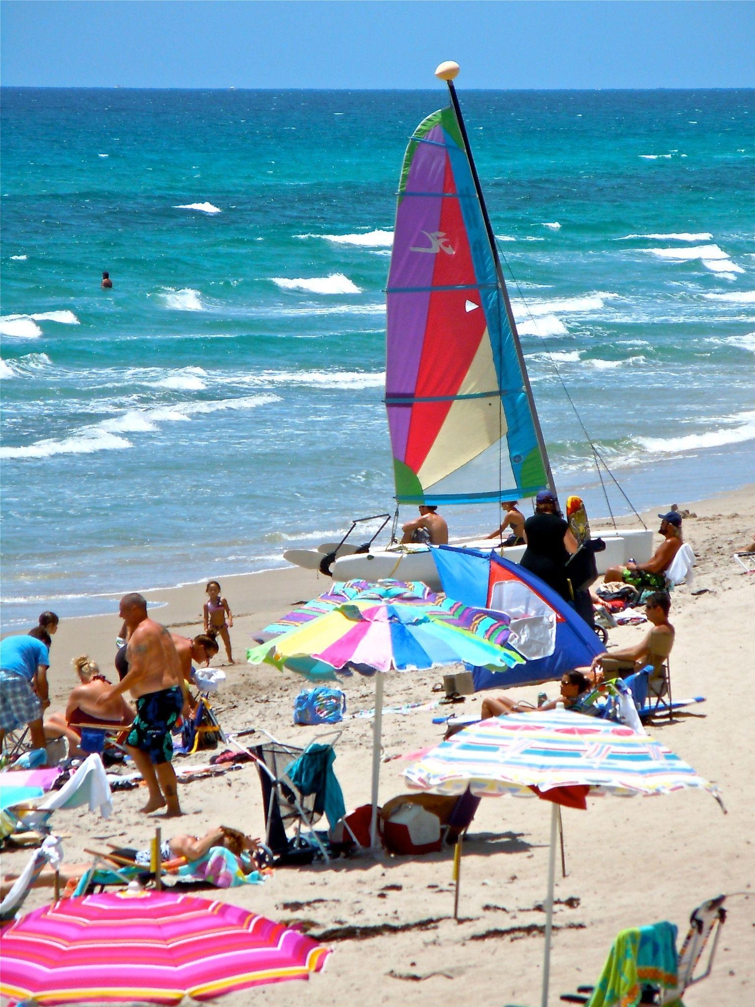 Lantana Public Beach with umbrellas, sailboat, and turquoise waves.
